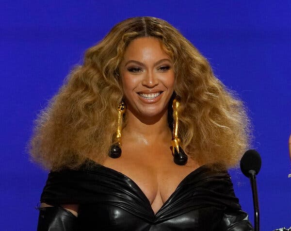 Beyoncé smiles widely at the Grammys podium, wearing a black dress with a plunging neckline.