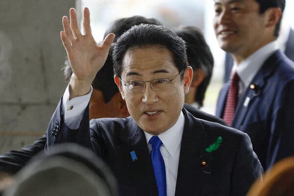 Fumio Kishida, in a dark suit, waving and smiling. 