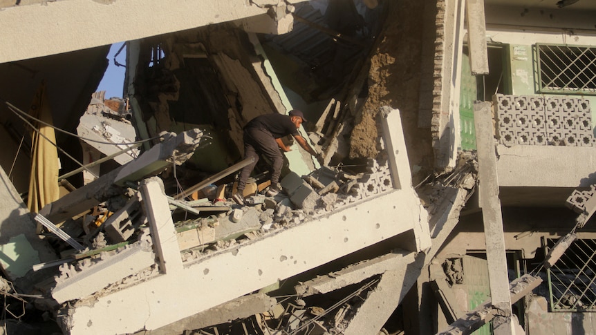 A man picks through broken concrete in a destroyed multi-level building