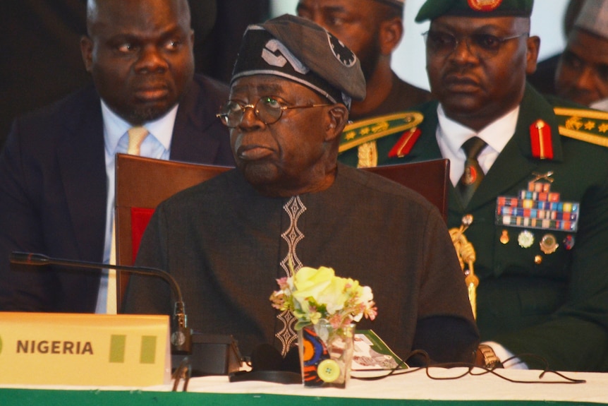 Bola Ahmed Tinubu wears black, placecard with "Nigeria" in front of him.