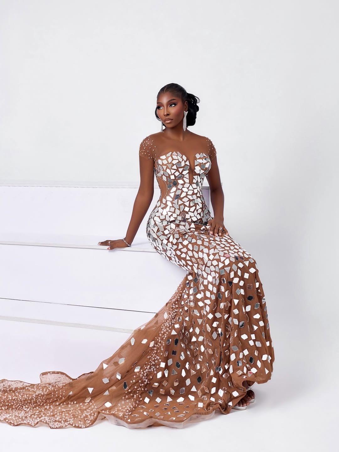 Tamunosoye Karibi George seated on white steps, wearing a sheer brown mermaid gown adorned with geometric mirror fragments for the talent performance segment.